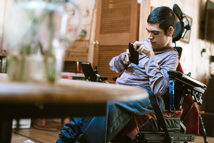 A cheerful young adult man with cerebral palsy researches texts someone on his smart phone, using voice recognition to aid in his communication.