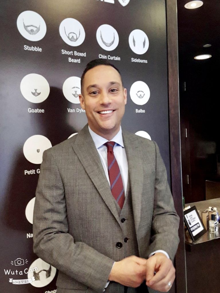 Man with dark hair smiling wearing grey suit with a red tie