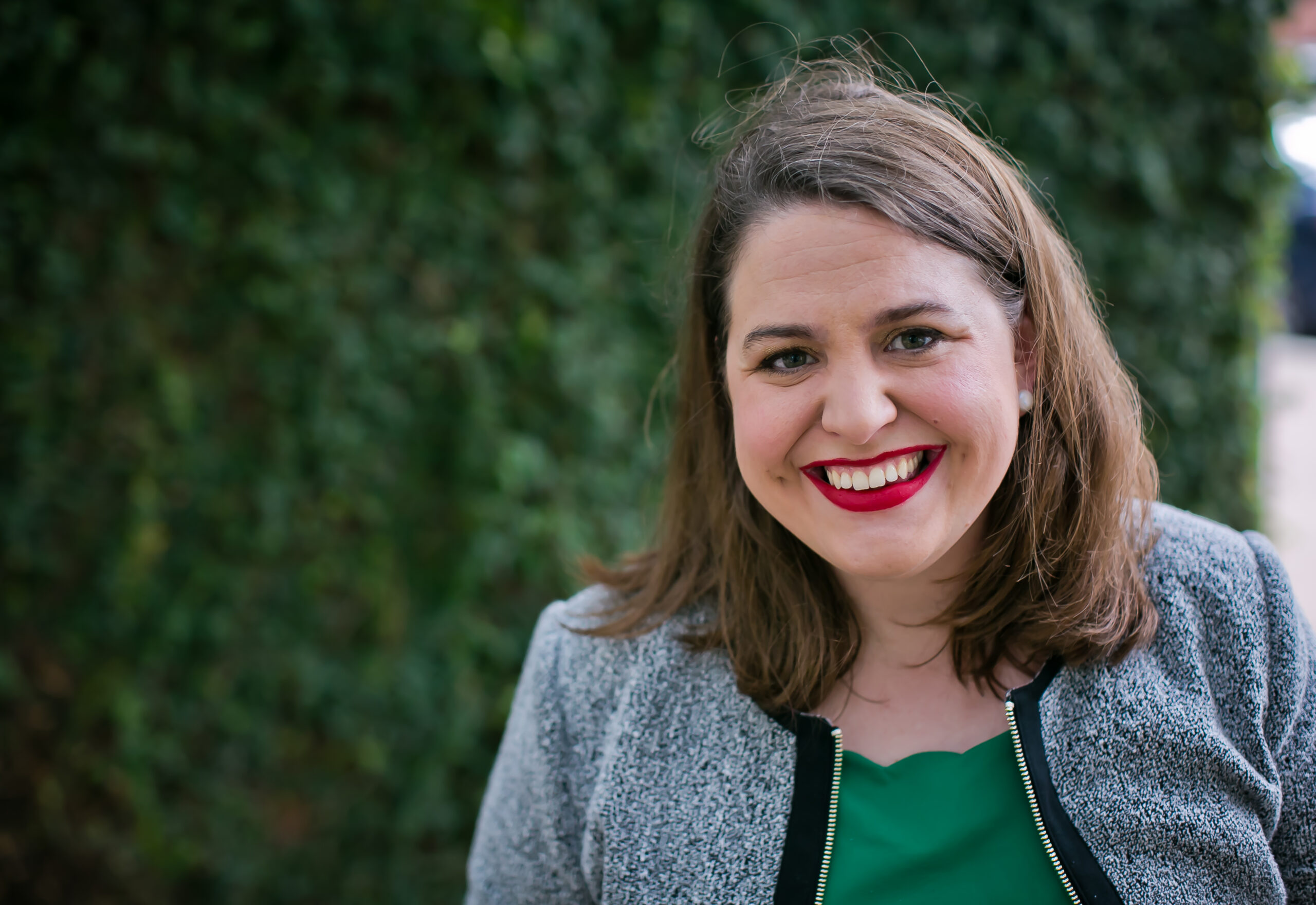 Woman with brown hair and red lipstick smiliing in front of green background.