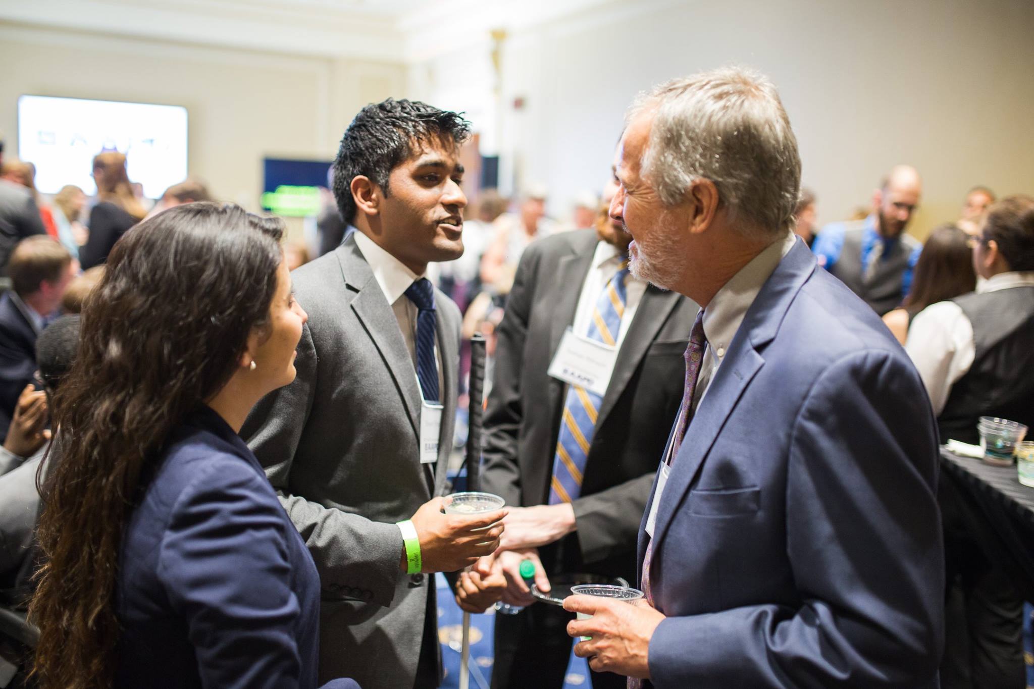 Two young people in suits shaking hands with an older man in a suit