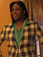 Black woman with dark hair smiling at camera with checkered jacket on.