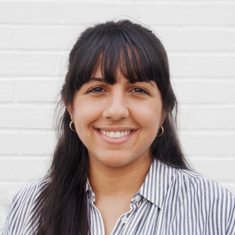 Headshot-with-Bangs-768x768 Headshot of a young brown woman with dark hair and bangs wearing small gold hoops and a striped blue and white shirt