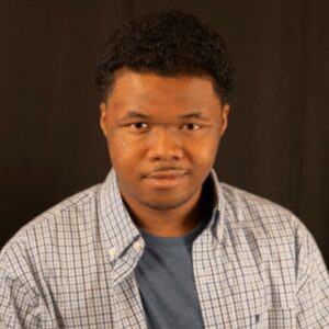 Man looking at camera with a slight smile wearing a checkered button down shirt with a grey t-shirt