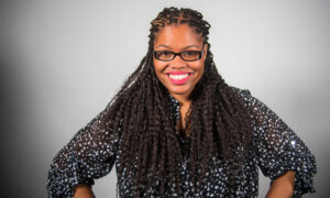 Woman with locs and glasses smiling with hands on hips 