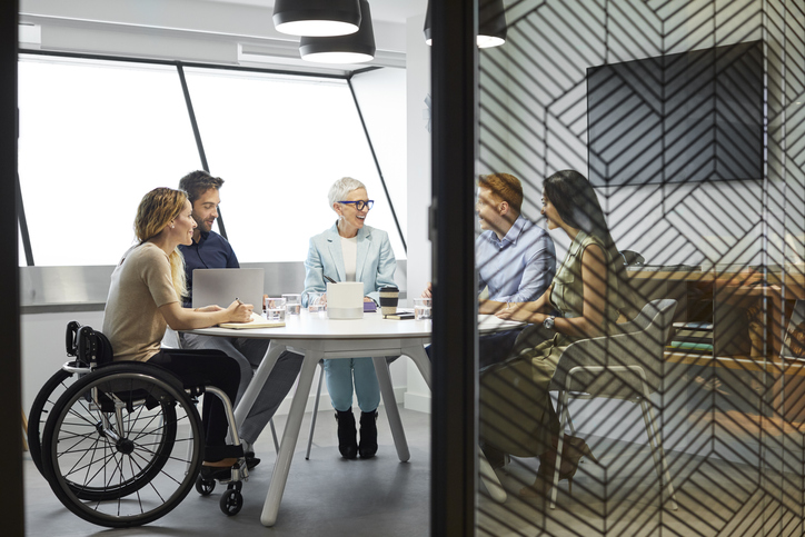Male and female professionals discussing in board room. Disabled businesswoman communicating with coworkers in meeting. They are at office.