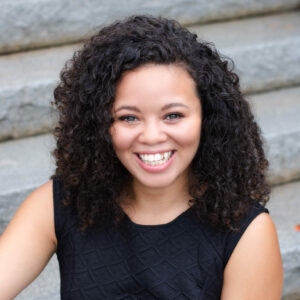 Woman with curly hair smiling at camera wearing black top