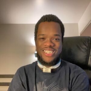 man looking at camera smiling wearing a black shirt with a white collar 