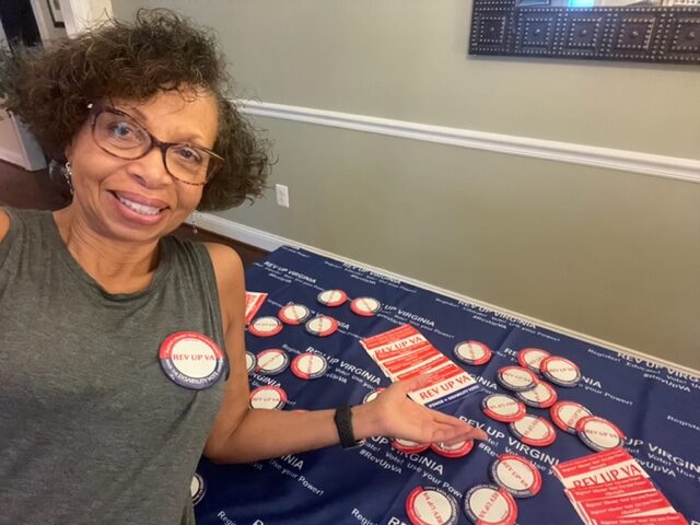 REV UP Virginia SWAG and Tablecloth Black woman wearing "I voted" sticker sitting in front of table full of Swag