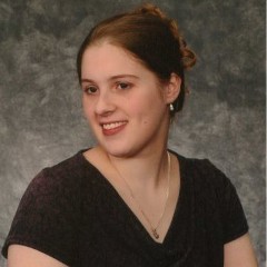 Photo of Sarah Blahovec with brown hair in an updo, wearing a black v-neck blouse