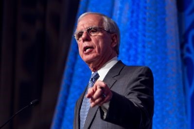 White man with glasses and grey hair wearing suit talking and pointing