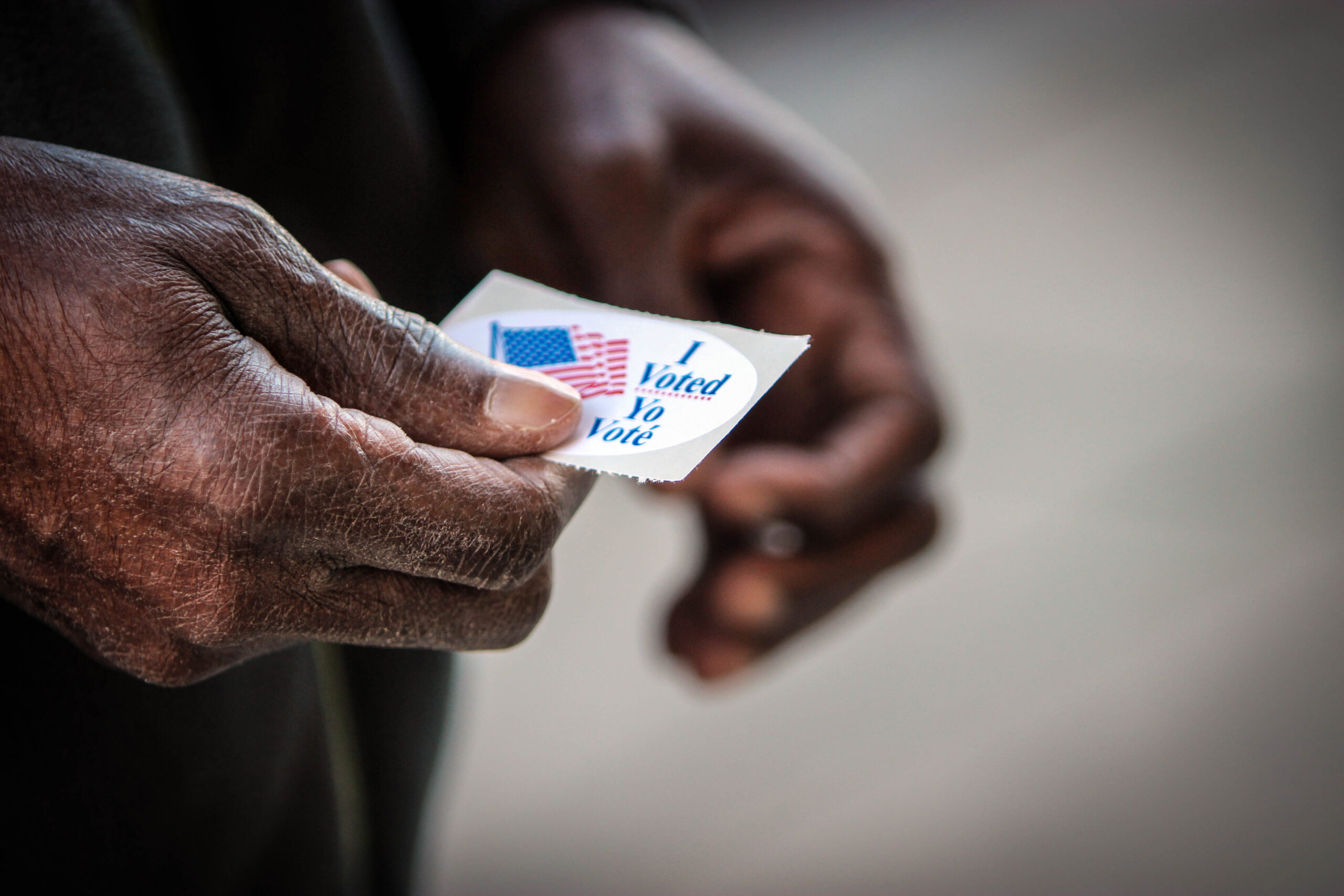 Hands of Black man holding an "I Voted" sticker.