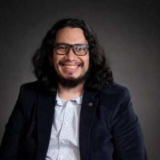 man with long hair smiling at camera wearing a white shirt and jacket sitting next to dog