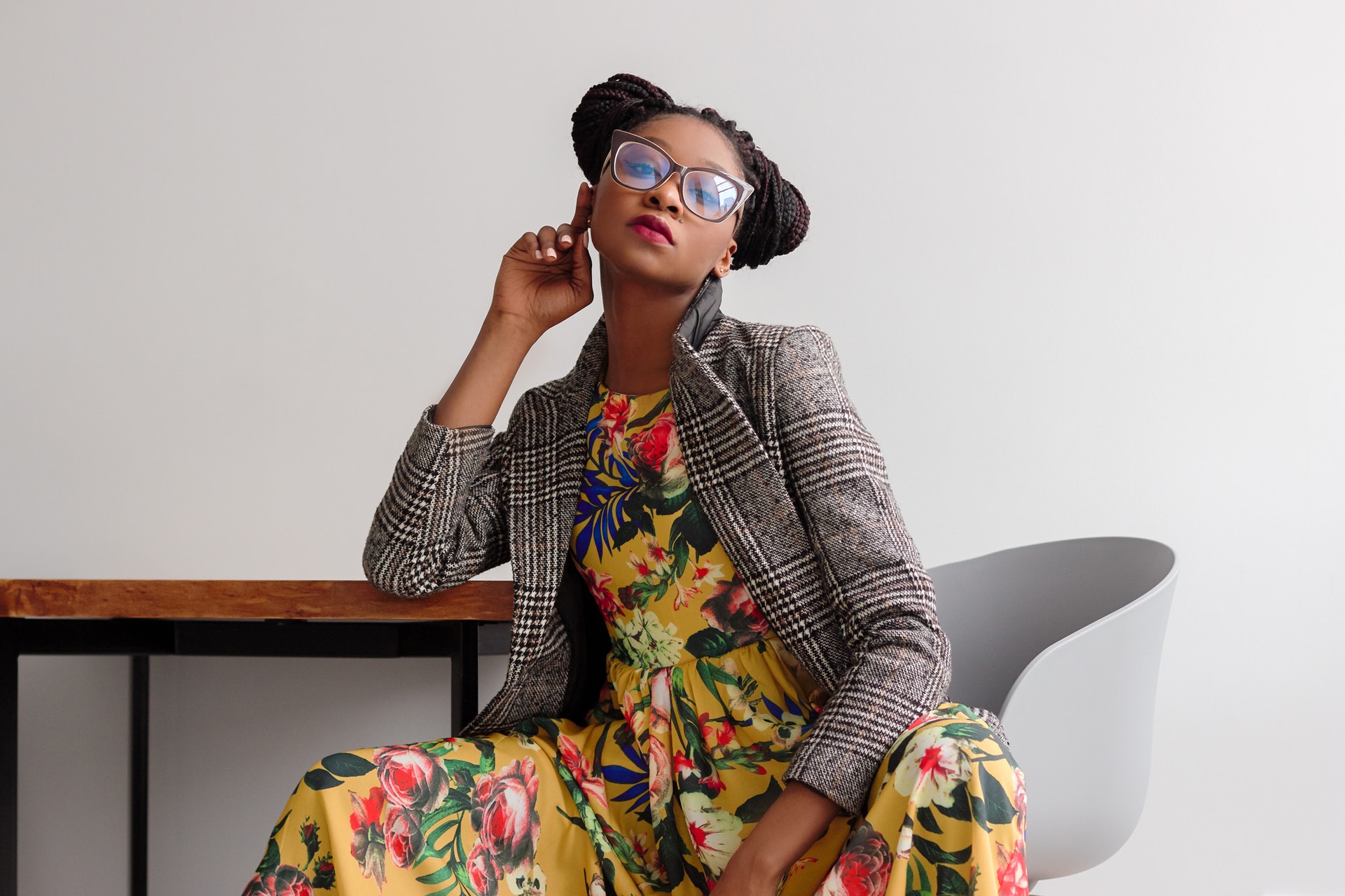 Black woman wearing glasses sitting in a floral dress with grey blazer