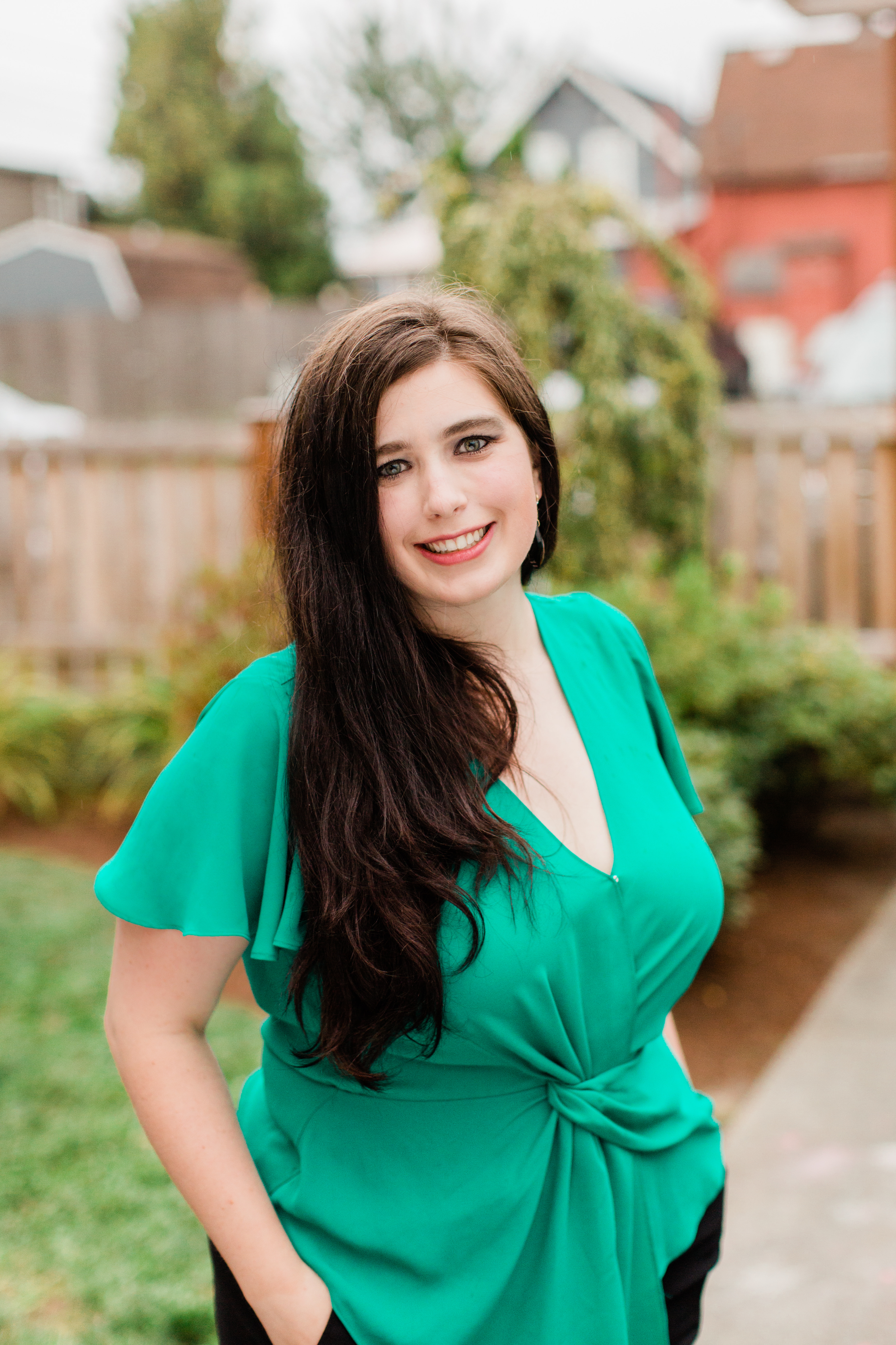 Woman with long brown hair wearing green top standing outdoors smiling