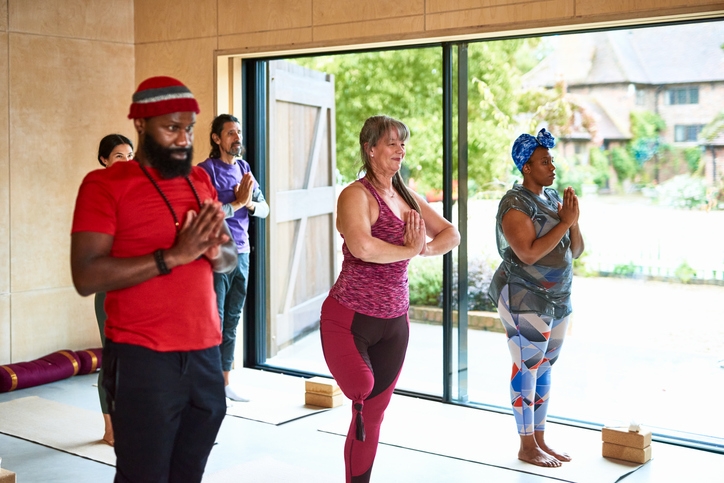 Multi ethnic yoga class standing with hands in prayer position, female amputee on one leg, focus, dedication, wellbeing