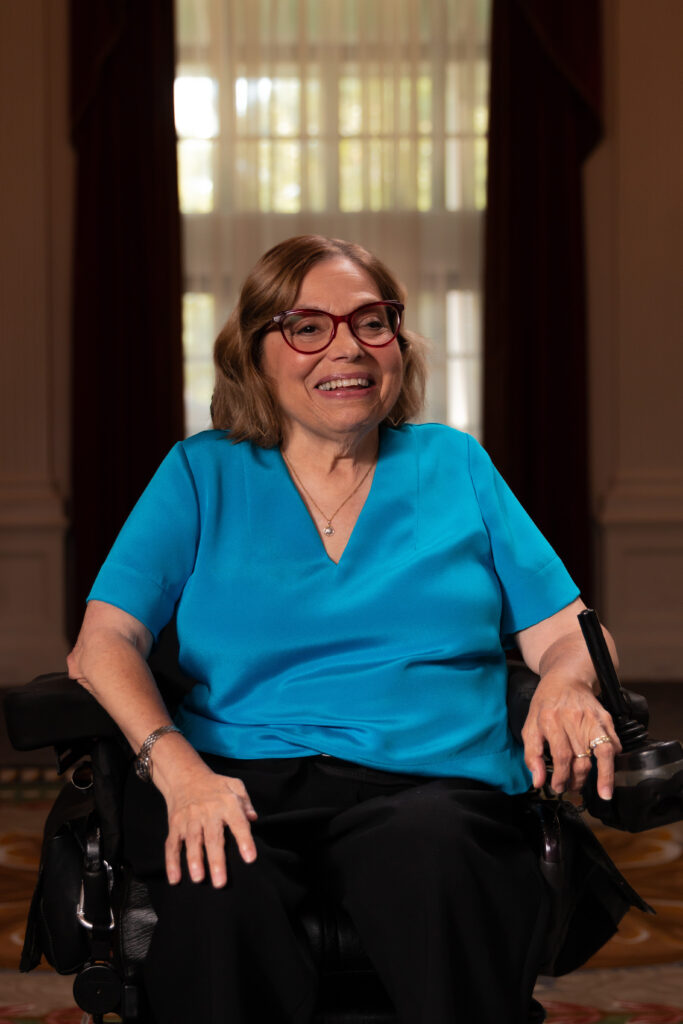 Judy Heumann speaks into a microphone at a 504 rally. She wears a sign 504 pin.