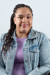 Headshot of Saphire Murphy, a bi-Racial woman with braids in a purple dress and jean jacket, seated in her power wheelchair.