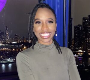 Smiling, black woman, locs pulled back, turtleneck sweater Chicago skyline behind