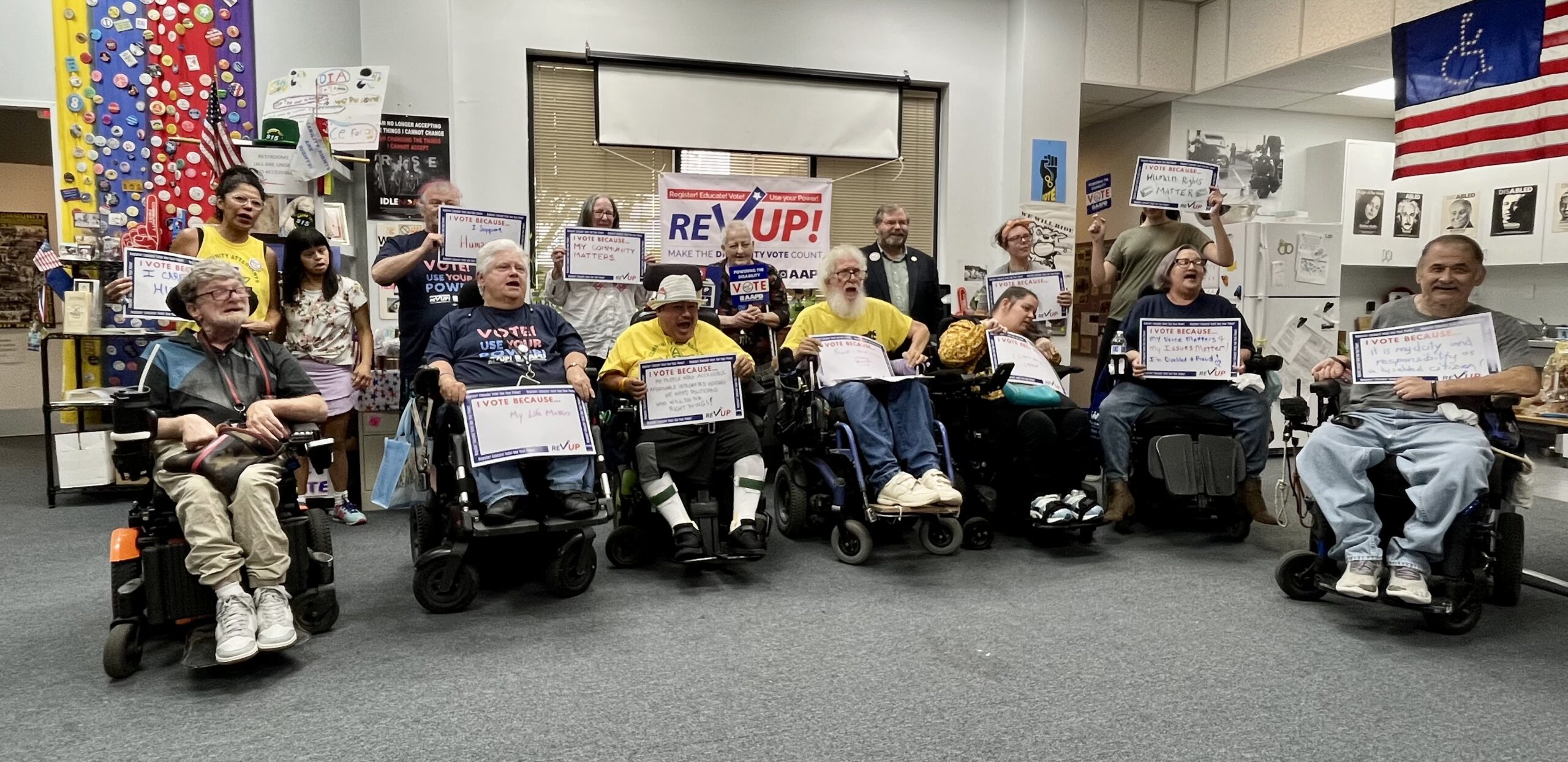 A group of advocates with disabilities are holding up voting advocacy signs in a room that looks like a political campaign office