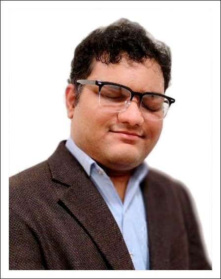 Maitreya Shah, an Asian Indian male with short curly hair wearing black glasses, a blazer and a button down shirt and is smiling.