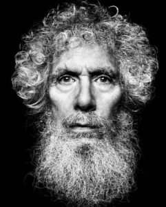 A portrait photograph of Bob Kafka, an older white man with curly white and grey hair and a beard. He has a serious, stoic expression on his face.