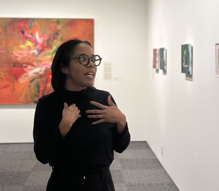 Lindsay discussing her art in front of a large orange painting called Solar Searching.