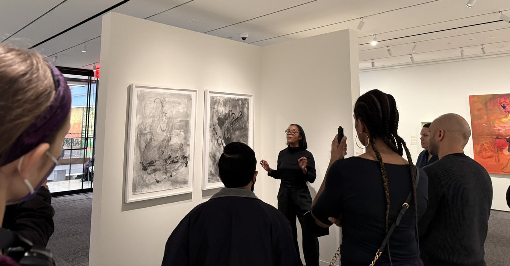 Lindsay Adams speaks to AAPD staff about her art. She’s standing in front of two untitled black-and-white works of art.