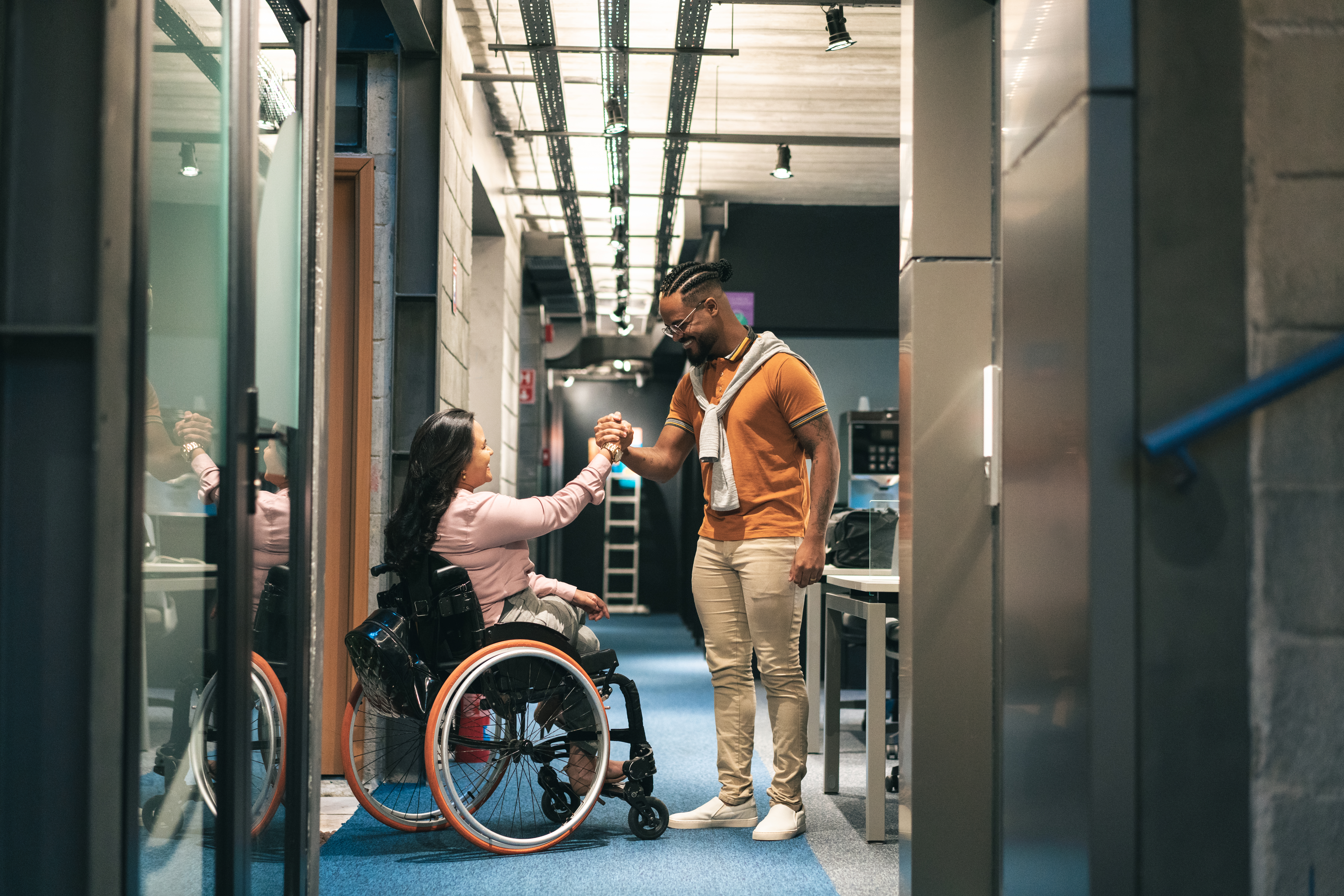 Two employees shaking hands, one of whom is a wheelchair user