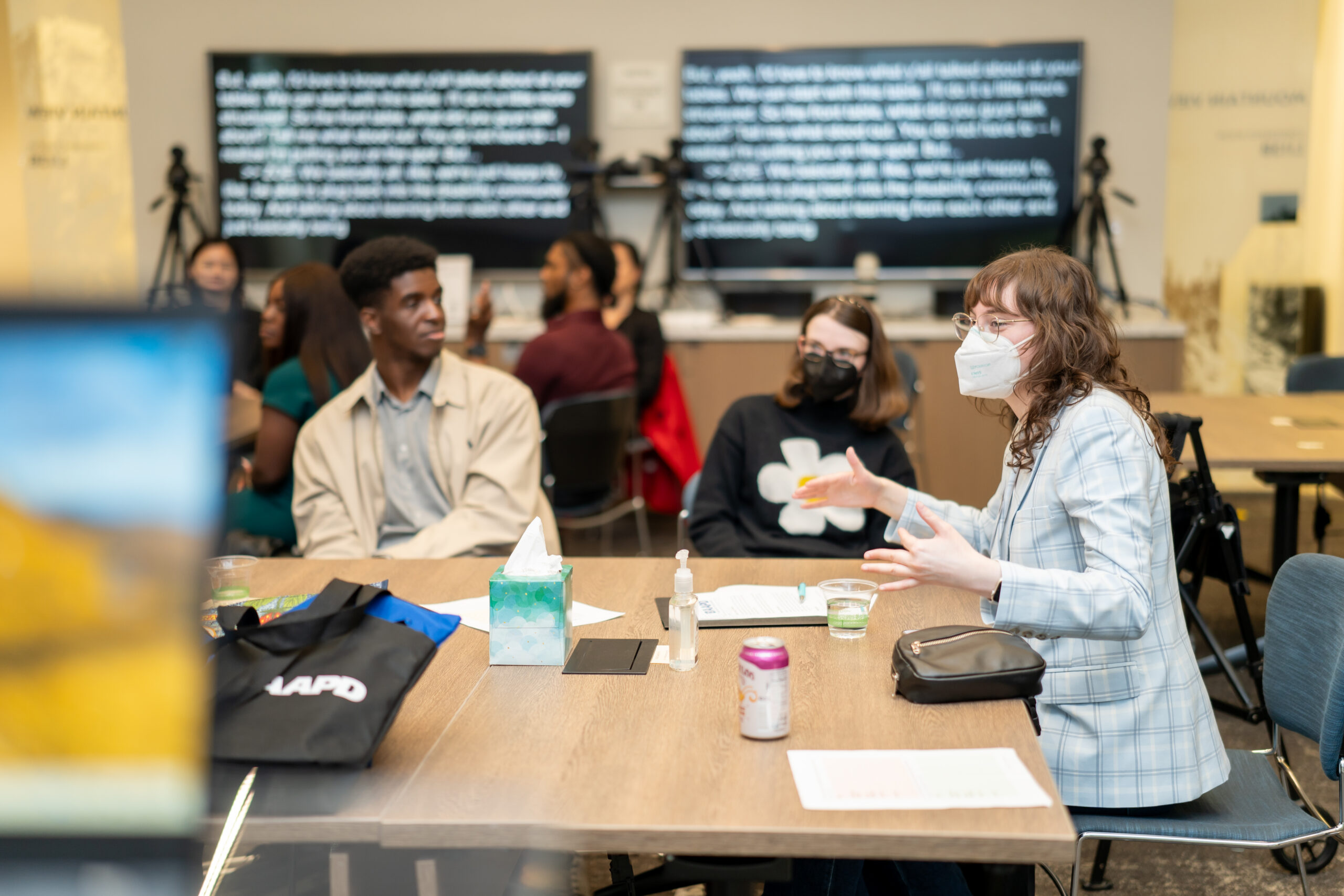 People sitting around a table while paying attention to someone speak. There is CART captioning behind them.