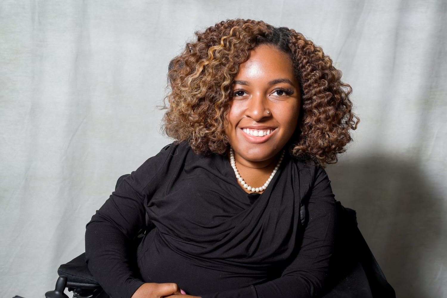 Gabrielle is a Black woman with medium brown skin. She has ombre curly hair that goes from black to brown. She is smiling and wearing a black blouse with a pearl necklace.